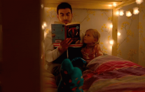 A man reading a book to a young girl on her bed with cosy lighting. He puts the book down and looks up, confusion on his face.