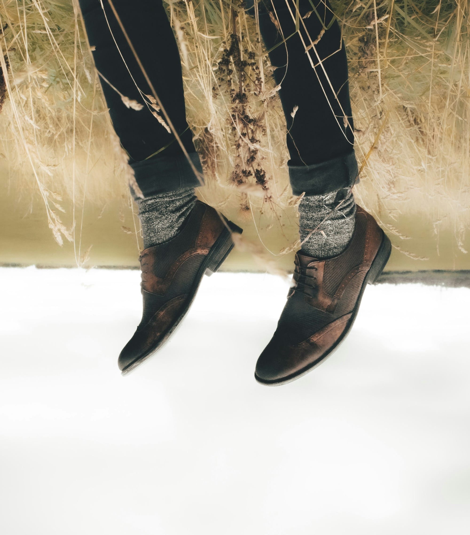 Upside-down image of legs in dark pants and brown shoes, appearing planted in dry grass, with the sky below.
