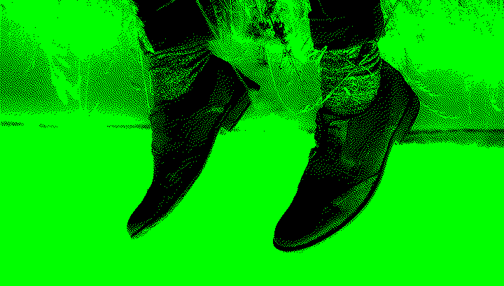 Upside-down image of legs in dark pants and brown shoes, appearing planted in dry grass, with the sky below.